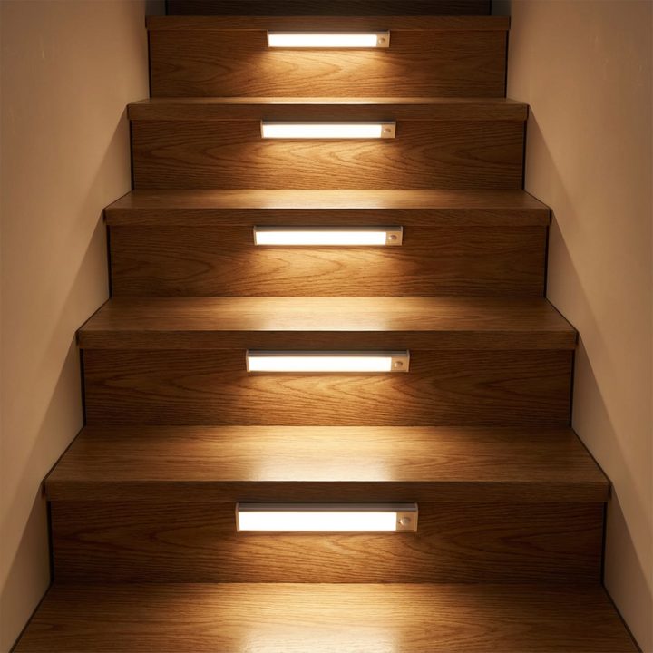 Vijf lichtbalken op de stootborden van een houten trap, die elke trede in warm licht zetten. 2