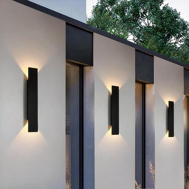 Drie zwarte wandlampen op een rij langs een lichte gevel, met zacht licht naar boven en beneden 12