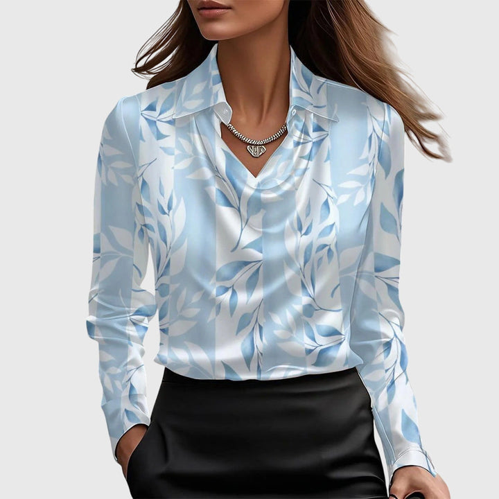 Model draagt de satijnen blouse met lichtblauw en wit bladerenpatroon, gedrapeerde hals en kraag, gecombineerd met een zwarte rok. 5