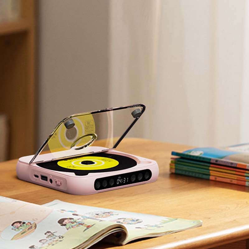 Roze cd-speler met geopende klep op een bureau, naast een opengeslagen kinderboek en een stapel boeken. 10