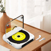 Witte cd-speler met geopende klep op een houten tafel naast een vaas en twee draadloze oordopjes. 8