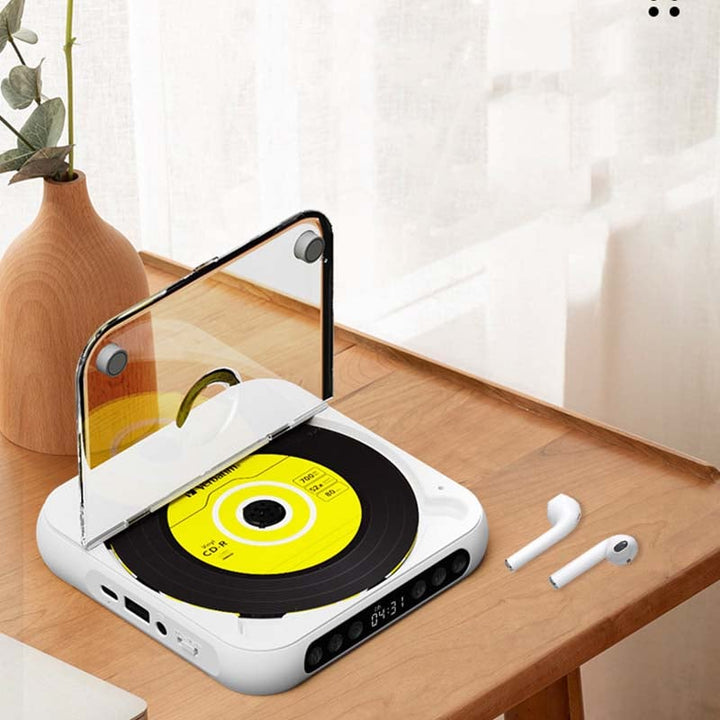 Witte cd-speler met geopende klep op een houten tafel naast een vaas en twee draadloze oordopjes. 8