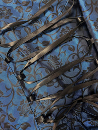 Close-up van de zwarte satijnen veterkoorden op blauwe stof met zwart bloemen- en rankenmotief. 5