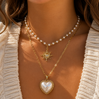 Model draagt de parelketting met zonhanger gelaagd boven een lange gouden schakelketting met hartvormige parelhanger. 3