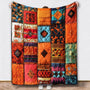 Deken met oranje, rode en turquoise patchwork-ontwerp met ruitvormen, omhooggehouden tegen een witte muur 3
