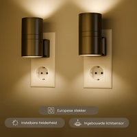 Twee zwarte cilindervormige stekkerlampen in stopcontacten verlichten een beige muur met warm licht 1