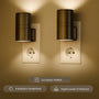 Twee zwarte cilindervormige stekkerlampen in stopcontacten verlichten een beige muur met warm licht 1