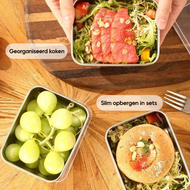 Bovenaanzicht van drie stalen bakjes op een houten tafel met zalmsalade, druiven en een broodje met salade. 8