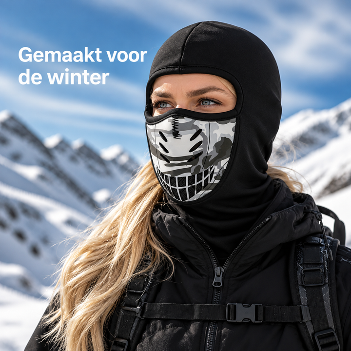 Vrouw met zwarte bivakmuts met camouflage-ventilatiepaneel voor de mond, tegen een besneeuwde bergachtergrond, gedragen met rugzak en jas. 1