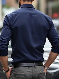 Achterkant van het marineblauwe overhemd aan een model, met schoudernaad en opgerolde mouwen, grijze broek 10