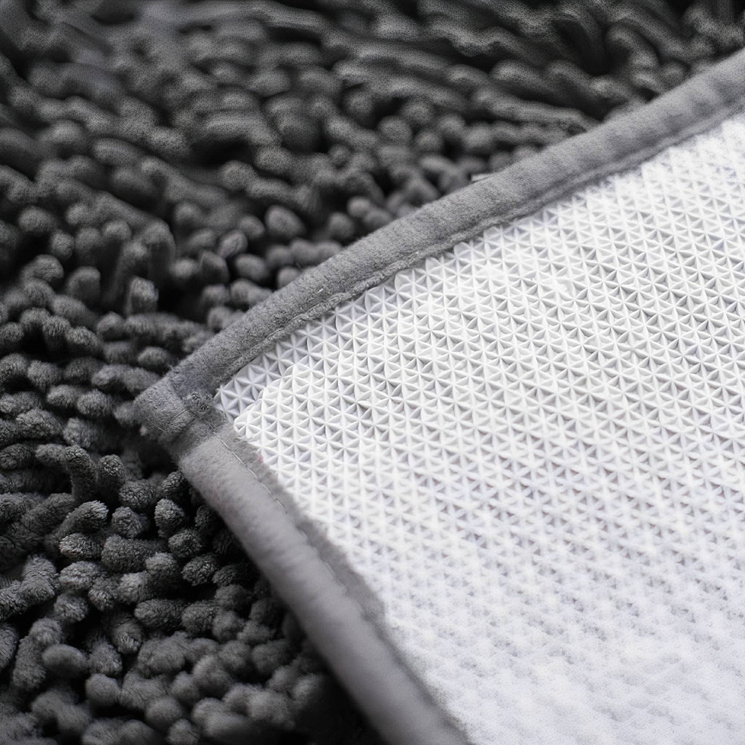 Onderkant van de mat met witte antislip noppenlaag en grijze omgenaaide rand naast de pluizige chenillekant. 8