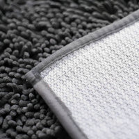 Onderkant van de mat met witte antislip noppenlaag en grijze omgenaaide rand naast de pluizige chenillekant. 8