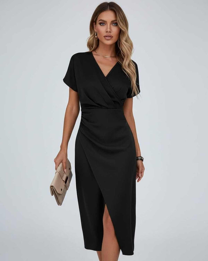 Model in zwarte midi-jurk met V-hals en split, met beige clutch in de hand 5