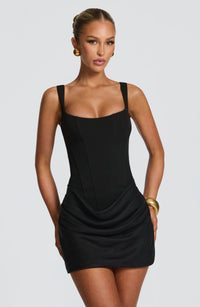 Close-up van de zwarte mini-jurk met vierkante hals en corsetbovenstuk, gedragen met gouden oorbellen. 10
