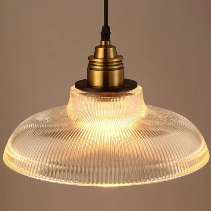 Close-up van één brandende hanglamp met doorzichtige geribbelde glazen kap en messingkleurige fitting 3
