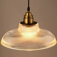 Close-up van één brandende hanglamp met doorzichtige geribbelde glazen kap en messingkleurige fitting 3
