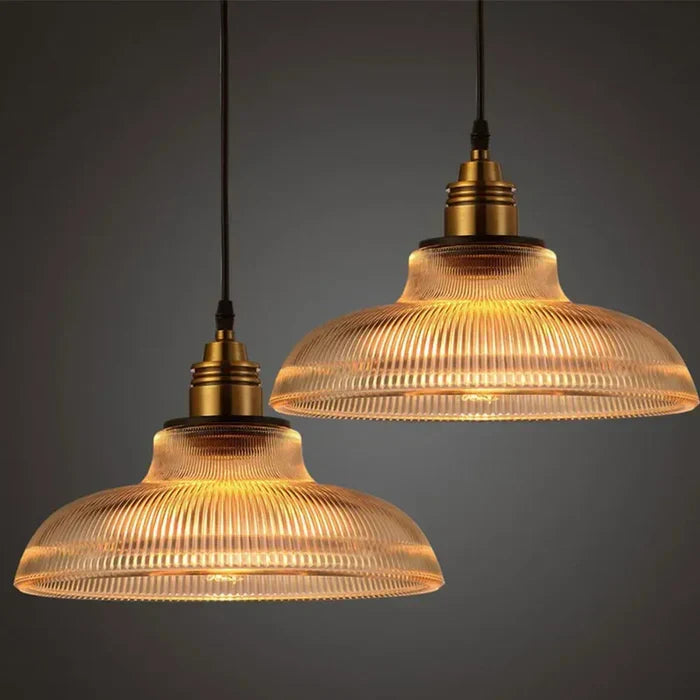Twee brandende hanglampen met geribbelde glazen kap en messingkleurige fitting voor een donkergrijze achtergrond 1