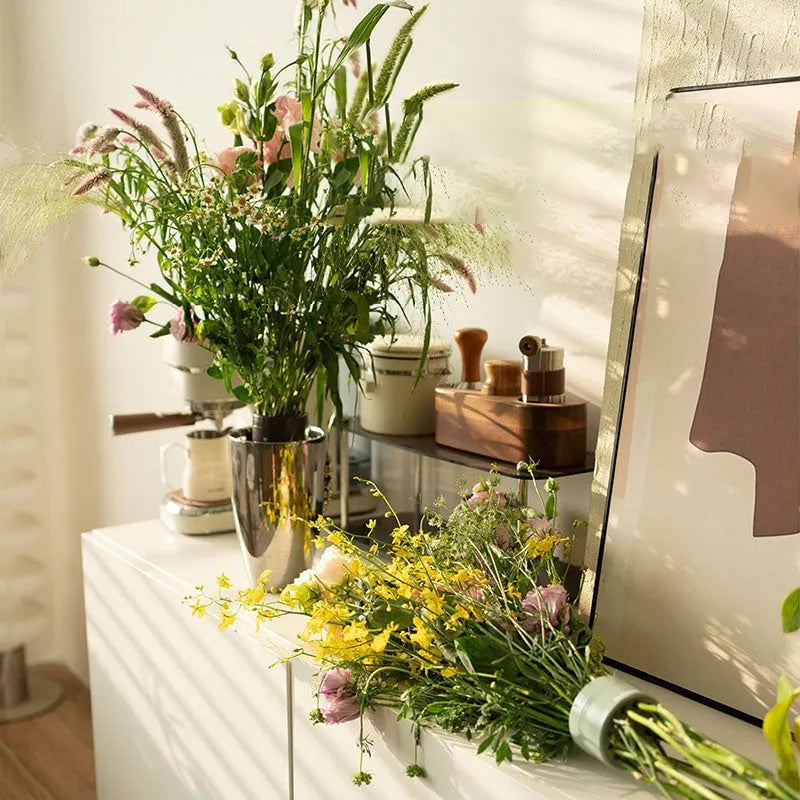 Wilde bloemen in een metalen vaas op een wit dressoir, met een tweede boeket met inzet ernaast. 3