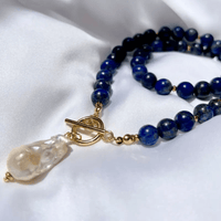 Ketting met blauwe kralen en gouden knevelsluiting op witte stof, de barokparel hangt links 5