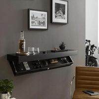 Zwarte wandplank aan een grijze muur in een woonkamer, met open vak vol spullen en een fles en glazen erbovenop. 4