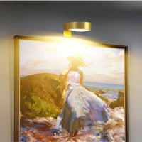 Gouden ronde lamp boven een ingelijst schilderij van een vrouw in jurk aan zee, warm verlicht 1