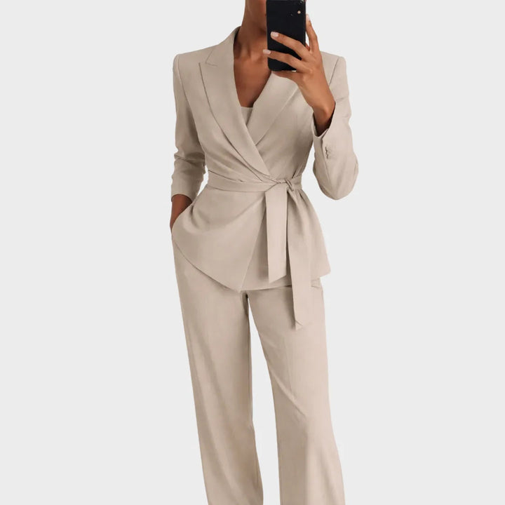 Dezelfde set in beige, gedragen door een model met telefoon in de hand, blazer met strikceintuur en wijde broek. 2