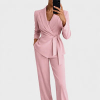 Dezelfde set in roze, gedragen door een model met één hand in de zak, blazer met overslag en strikceintuur. 4