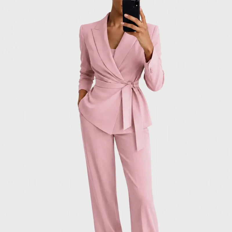 Dezelfde set in roze, gedragen door een model met één hand in de zak, blazer met overslag en strikceintuur. 4