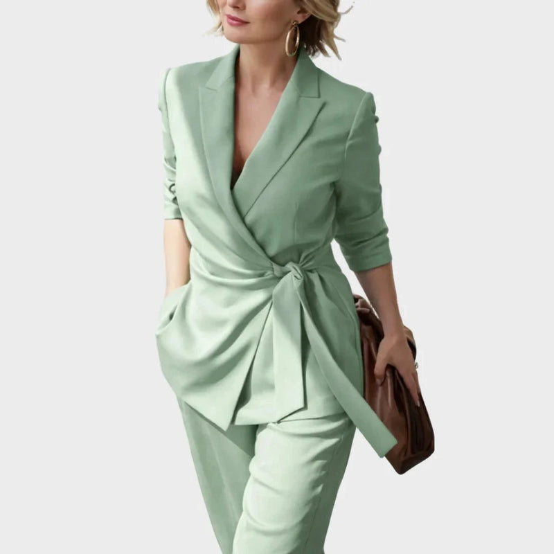 Close-up van de mintgroene blazer met de geknoopte ceintuur op de heup, gedragen door een model met bruine tas en oorringen. 6