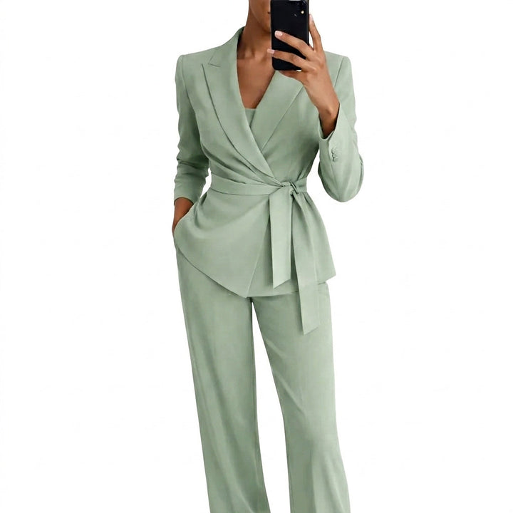 Model in mintgroen kostuum met overslagblazer, ceintuur in een strik en wijde broek, neemt een spiegelselfie met telefoon. 1