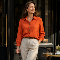 Oranje blouse met houten knopen, gedragen door een glimlachende vrouw met beige broek en riem 17