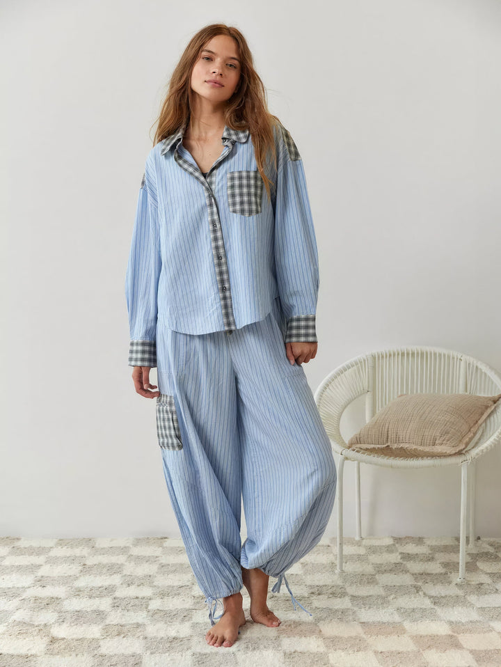 Model in volledige blauw gestreepte set met grijs geruite details, broek met opgenomen zoom met koordjes en zijzak, op blote voeten. 7
