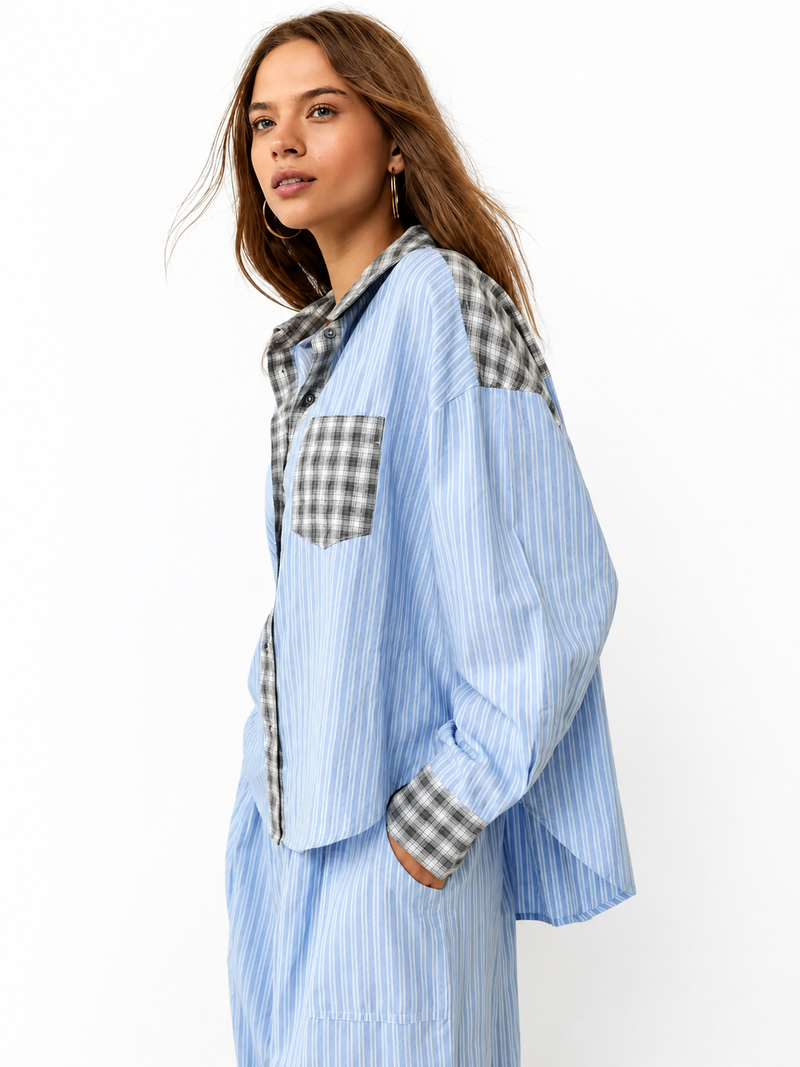 Model in blauw gestreept pyjamaoverhemd met grijs geruite kraag, borstzak en manchetten, zijaanzicht met een hand in de zak, tegen witte achtergrond. 1