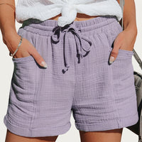 Dezelfde short in lila, gedragen door een model met handen in de zakken, met zichtbare trekkoordstrik en omgeslagen zomen. 2
