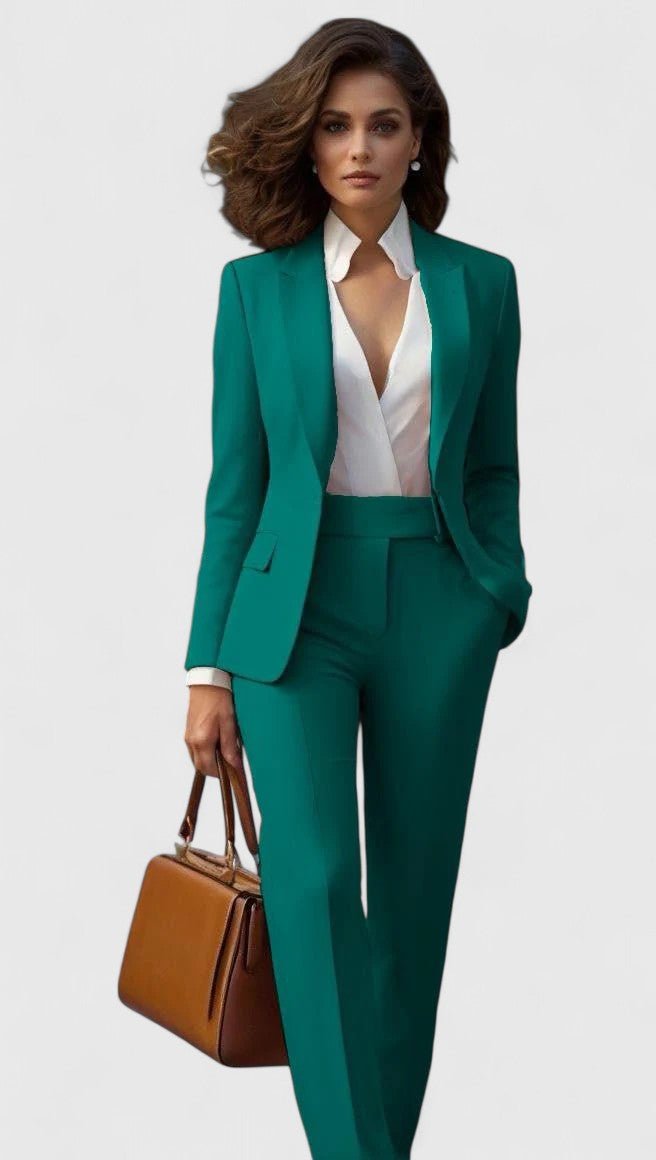 Model draagt het kostuum in smaragdgroen, gecombineerd met een witte blouse en een bruine leren handtas. 4