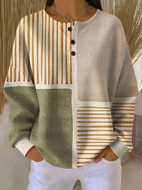 Wafeltrui met knoopjes aan de hals en kleurblokken in groen, beige en bruingeel gestreept, gedragen met witte broek. 1