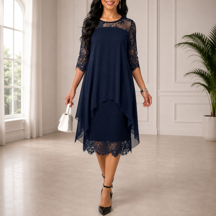 Model draagt de jurk in marineblauw met kanten mouwen en schouderstuk in een lichte zaal 1
