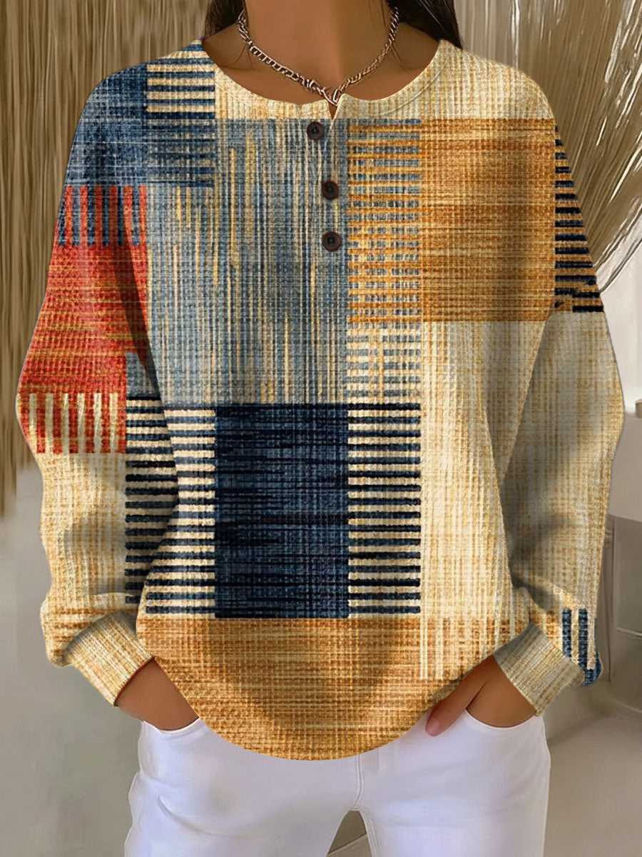 Wafeltrui met knoopjes en blokpatroon met strepen in blauw, oranje, rood en beige, gedragen met witte broek. 3