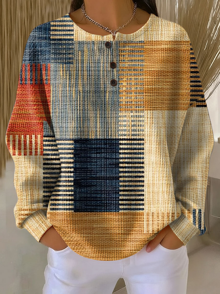 Wafeltrui met knoopjes en blokpatroon met strepen in blauw, oranje, rood en beige, gedragen met witte broek. 3