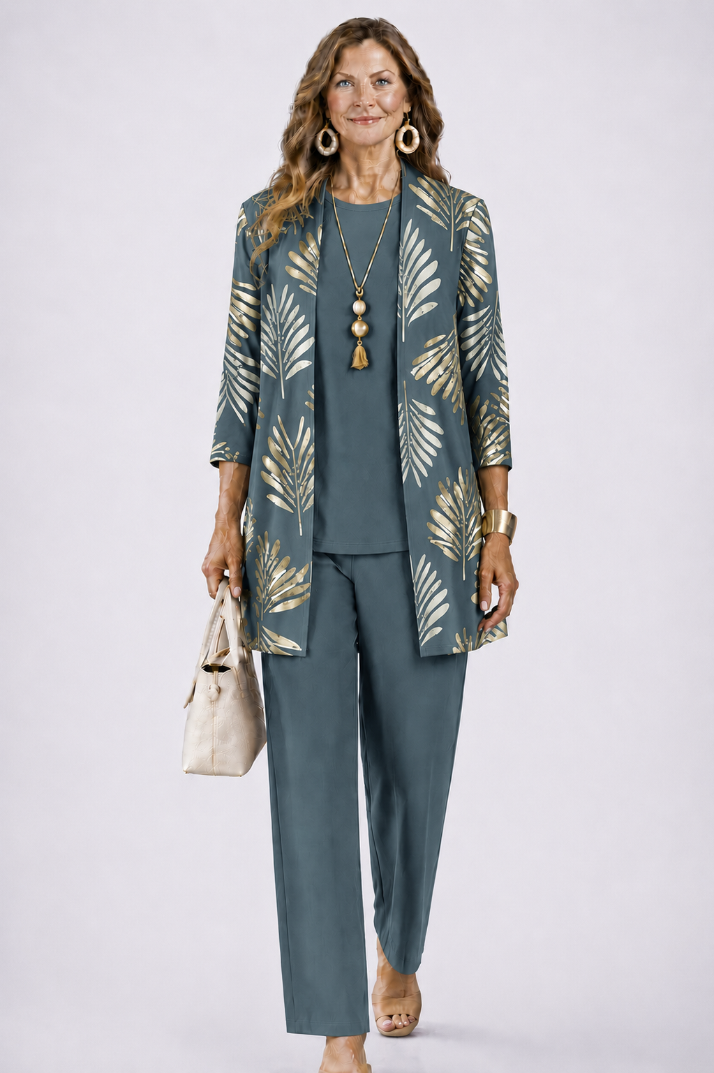Model in grijsblauwe set met gouden bladprint op het open vest, gedragen met effen top, broek en beige tas. 1