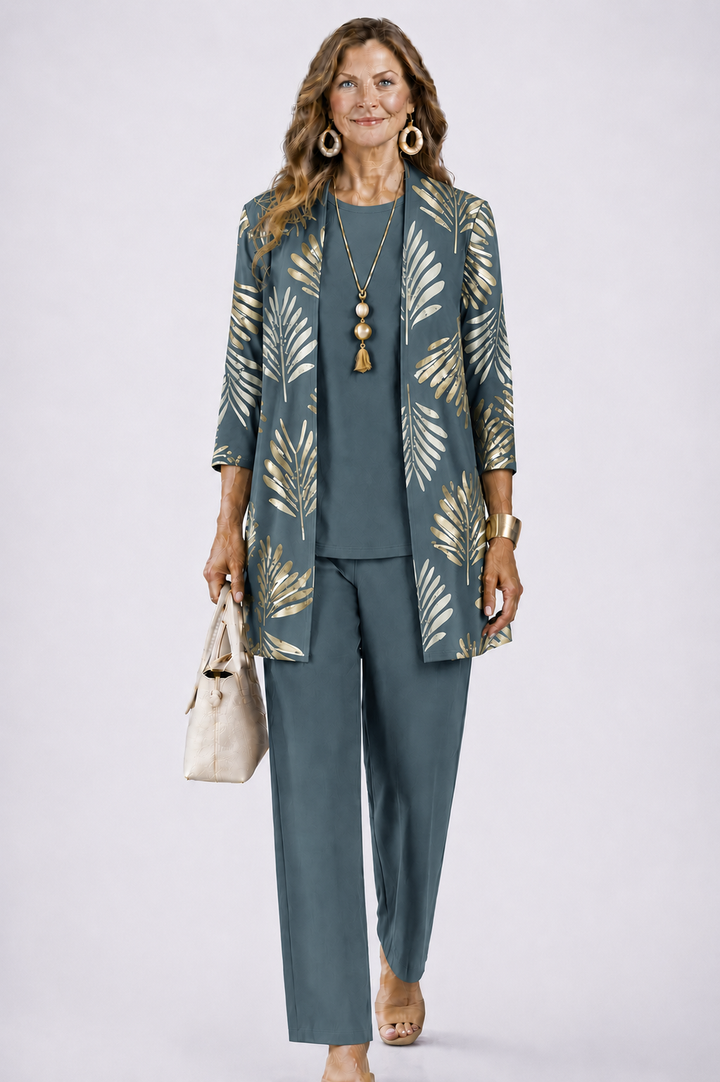 Model in grijsblauwe set met gouden bladprint op het open vest, gedragen met effen top, broek en beige tas. 1