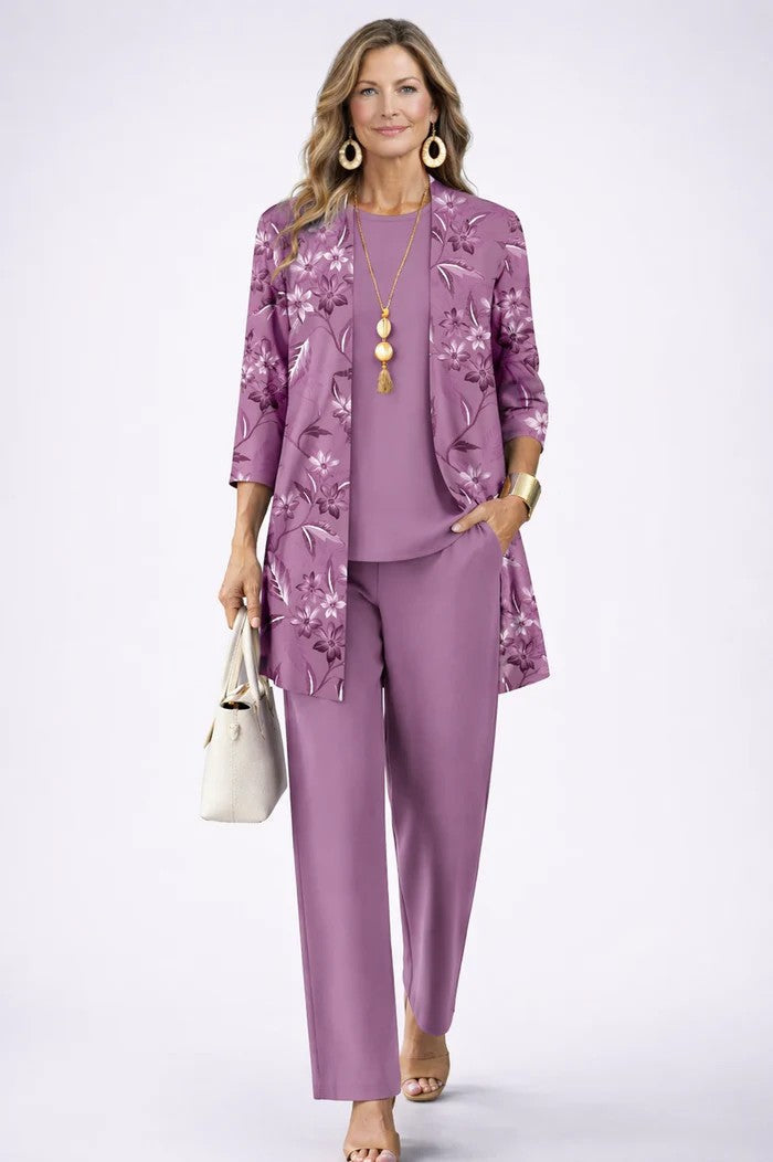 Model in lila set met bloemenprint op het open vest, effen top en broek, hand in de zak. 11