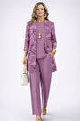 Model in lila set met bloemenprint op het open vest, effen top en broek, hand in de zak. 11