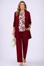 Model in rood open vest en broek met witte top met rode bloemenprint, beige handtas in de hand. 13