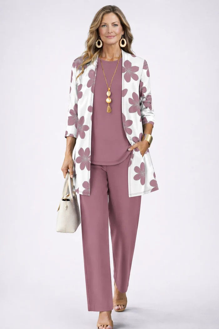 Model in mauve top en broek met wit open vest met grote mauve bloemen, hand in de zak. 18