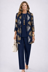 Model in donkerblauwe set met gouden bladprint op het open vest, effen top en broek, beige tas in de hand. 7