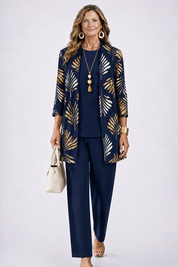 Model in donkerblauwe set met gouden bladprint op het open vest, effen top en broek, beige tas in de hand. 7