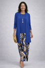 Model in effen blauw lang vest en top, gecombineerd met broek met abstracte blauw-bruine print en strogele clutch. 9