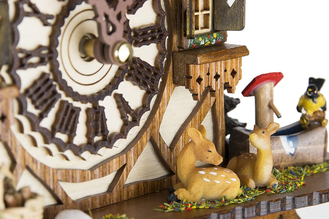Close-up van twee hertenkalfjes op kunstgras naast een rode paddenstoel, een gele vogel en het uitgesneden houten klokwerk. 15