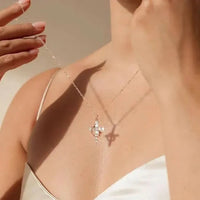 Vrouw in witte top houdt een fijne ketting met kruishanger met kleine steentjes omhoog, de hanger werpt een schaduw op haar huid. 1